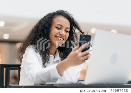 smiling young woman communicating via video link sitting at a table in a cafe . 79697488