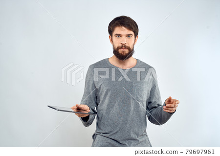 A man in a gray sweater a tablet in the hands of emotions Internet technology lifestyle light background A man in a gray sweater a tablet in the hands of emotions Internet technology lifestyle light background 79697961