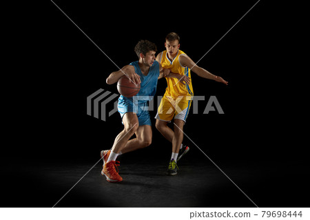 Two basketball players in action and motion isolated on dark black studio background. Advertising concept. Strong Caucasian athletes practicing with basketball ball. Two basketball players in action and motion isolated on dark black studio background. Advertising concept. Strong Caucasian athletes practicing with basketball ball. 79698444