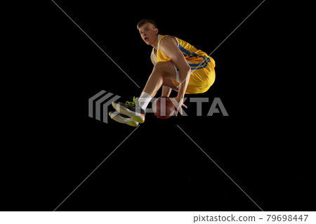 Jump shot. Basketball player with a ball in action and motion isolated on dark black studio background. Advertising concept. Strong Caucasian athlete practicing with basketball ball. Jump shot. Basketball player with a ball in action and motion isolated on dark black studio background. Advertising concept. Strong Caucasian athlete practicing with basketball ball. 79698447