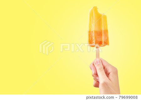 Bitten red frozen fruit ice cream popsicle in woman hand on yellow background 79699008