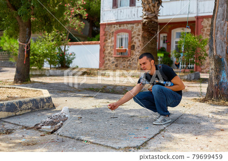 The guy feeds the seagulls with bread on the embankment The guy feeds the seagulls with bread on the embankment 79699459