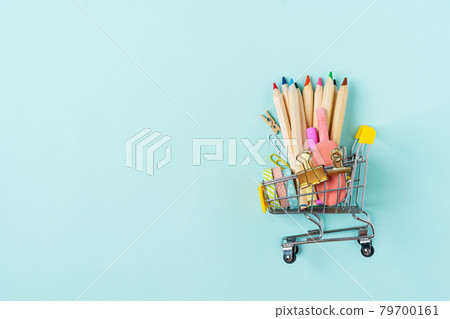 Buying school supplies, pencils, tape, notebook and crayons. Stationery for kids in a shopping cart on blue turquoise background, copy space. Back to school concept. Flat lay top view. Buying school supplies, pencils, tape, notebook and crayons. Stationery for kids in a shopping cart on blue turquoise background, copy space. Back to school concept. Flat lay top view. 79700161