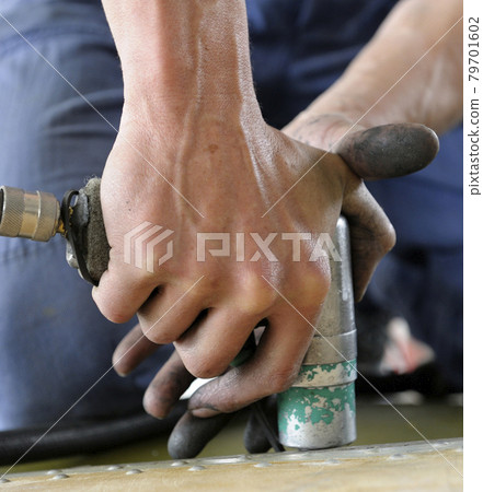 Worker hands making holes with a pneumatic drill on the body plane for further riveting 79701602