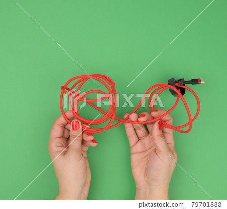 female hand holds twisted cable for charging mobile devices in a red textile wrapper on a green background female hand holds twisted cable for charging mobile devices in a red textile wrapper on a green background 79701888