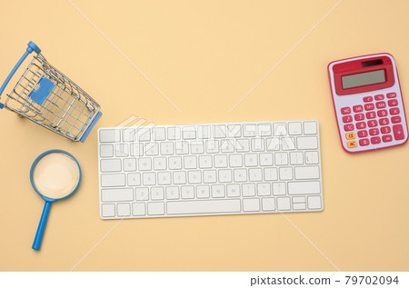 white wireless keyboard and empty shopping cart, magnifier on beige background, budget analysis concept 79702094