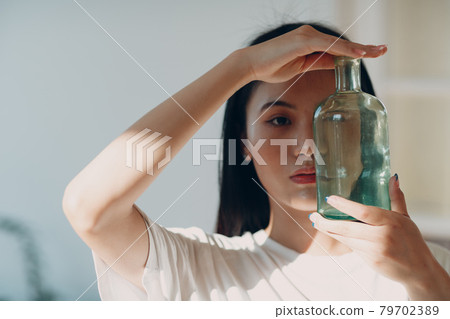 Asian young adult woman hold green glass bottle front face with day sunlight Asian young adult woman hold green glass bottle front face with day sunlight 79702389