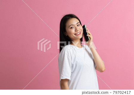 Smiling asian woman speaking mobile phone standing on pink background. Smiling asian woman speaking mobile phone standing on pink background. 79702417