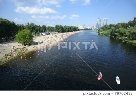 View of the Dnipro river, crowd of people sunbathing on the sandy beach and swimming in the water. Hydropark, Kyiv, Ukraine 79702452