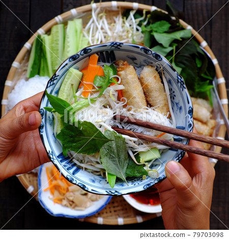people eating Vietnamese vegan food, rice noodle, fried spring rolls hand hold noodle bowl 79703098
