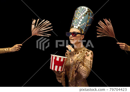 One young woman in image of Nefertiti in art performance watching movie isolated on dark background. Retro style, comparison of eras, humor concept. 79704423