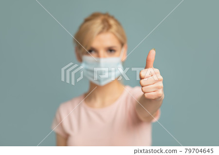 Woman in medical protective mask showing thumb up on grey studio background. Stay safe and healthy during pandemic Woman in medical protective mask showing thumb up on grey studio background. Stay safe and healthy during pandemic 79704645