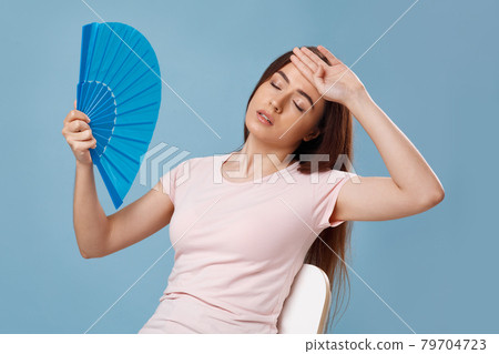 Closeup of overheated young lady sitting on chair with fan Closeup of overheated young lady sitting on chair with fan 79704723