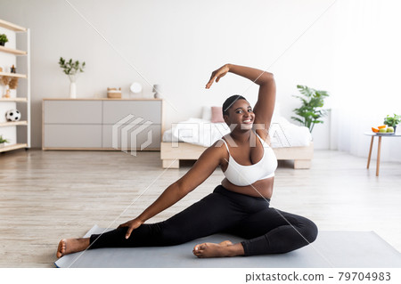 Full length of overweight black lady stretching her body, bending aside on yoga mat, leading active lifestyle at home Full length of overweight black lady stretching her body, bending aside on yoga mat, leading active lifestyle at home 79704983