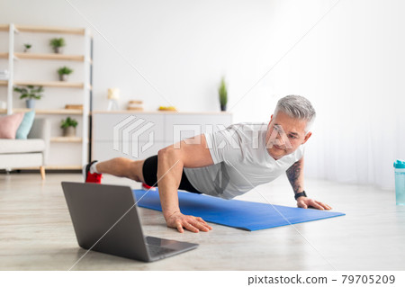 Fit mature man in sportswear doing push-ups, using laptop, having online fitness class from home, copy space Fit mature man in sportswear doing push-ups, using laptop, having online fitness class from home, copy space 79705209