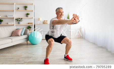 Strength workout concept. Active mature man doing squats at home, exercising in living room, panorama, free space 79705289