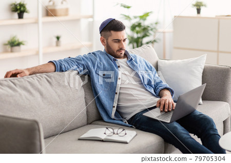 Jewish man working on computer, sitting on couch Jewish man working on computer, sitting on couch 79705304