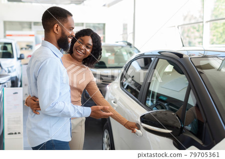 Car Choosing. Happy Black Spouses Standing Next To Modern Vehicle In Showroom Car Choosing. Happy Black Spouses Standing Next To Modern Vehicle In Showroom 79705361