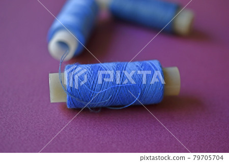 Blue spools of thread on a purple background with needles 79705704