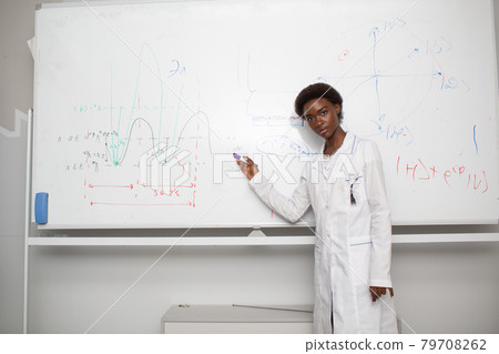 African American woman math teacher stands at blackboard with marker 79708262