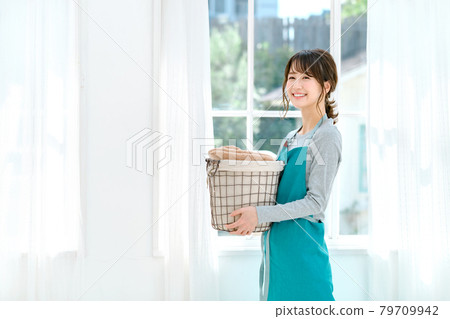 A young housewife in an apron doing housework at home (laundry) A young housewife in an apron doing housework at home (laundry) 79709942