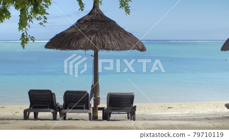 View of empty chaise-longue near native sun umbrella against blue water, Mauritius Island View of empty chaise-longue near native sun umbrella against blue water, Mauritius Island 79710119