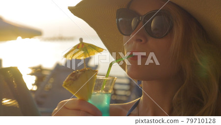Woman in Hat and Sunglasses Drinking Cocktail 79710128