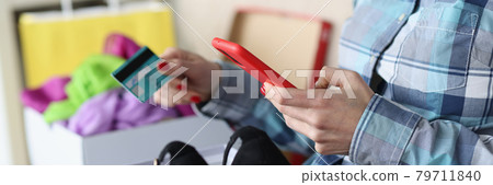 Woman is sitting on couch with box of shoes and holding bank card and smartphone Woman is sitting on couch with box of shoes and holding bank card and smartphone 79711840