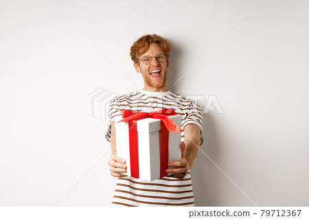 Valentines day and holidays concept. Happy redhead man smiling and giving you gift box, congratulating with birthday, standing over white background 79712367