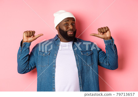 Confident and cheeky Black man pointing at himself, staring at camera self-assured, show-off, standing over pink background Confident and cheeky Black man pointing at himself, staring at camera self-assured, show-off, standing over pink background 79713657