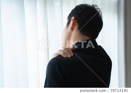 Back view of a man standing by a window with his hand on his shoulder 79714195