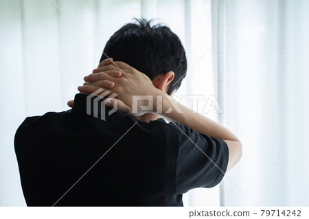 一名男子雙手放在脖子上站在窗邊的後方視圖 79714242