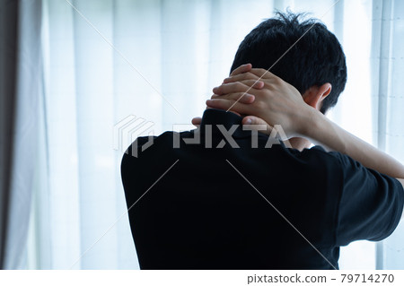 Back view of a man standing by a window with his hands on his neck 79714270