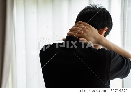 Back view of a man standing by a window with his hands on his neck Back view of a man standing by a window with his hands on his neck 79714271