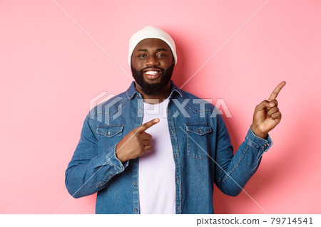 Happy african-american man smiling, pointing fingers right and showing promo, making announcement, standing over pink background 79714541