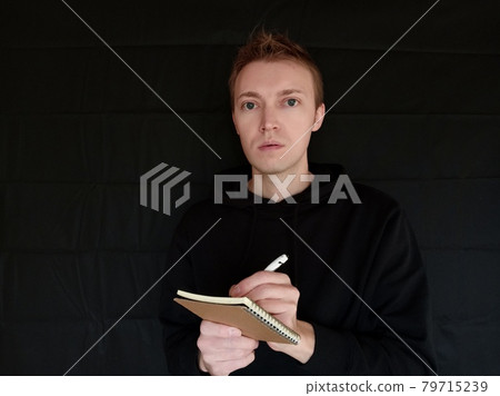 Foreign man taking notes with a ballpoint pen on a black background Foreign man taking notes with a ballpoint pen on a black background 79715239