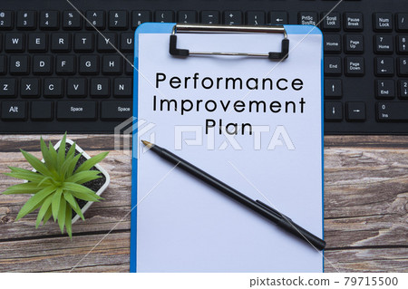 Text on blue clipboard on top of a keyboard with pen and potted plant on wooden desk Text on blue clipboard on top of a keyboard with pen and potted plant on wooden desk 79715500