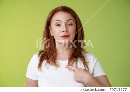 Proud mom pointing herself. Motivated confident redhead assertive middle-aged woman indicating chest volunteering bragging own abilities achievements look camera self-assured green background 79715577