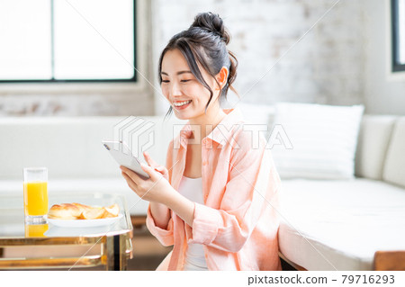 年輕女子在客廳吃早餐時看著智慧型手機 年輕女子在客廳吃早餐時看著智慧型手機 79716293