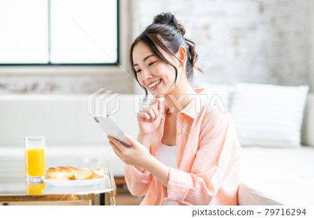 年輕女子在客廳吃早餐時看著智慧型手機 年輕女子在客廳吃早餐時看著智慧型手機 79716294