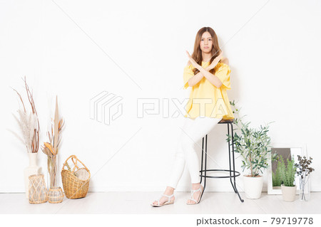 A young woman sitting on a chair in front of a white wall and making an NG gesture A young woman sitting on a chair in front of a white wall and making an NG gesture 79719778