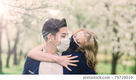 Young loving couple walking in medical masks in the park during quarantine on their wedding day. Young loving couple walking in medical masks in the park during quarantine on their wedding day. 79720010