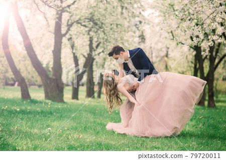 Young loving couple in medical masks in park during quarantine on wedding day. Young loving couple in medical masks in park during quarantine on wedding day. 79720011