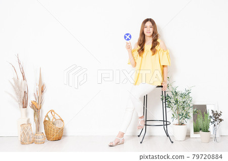 A young woman sitting on a chair in front of a white wall and holding a "No" placard 79720884