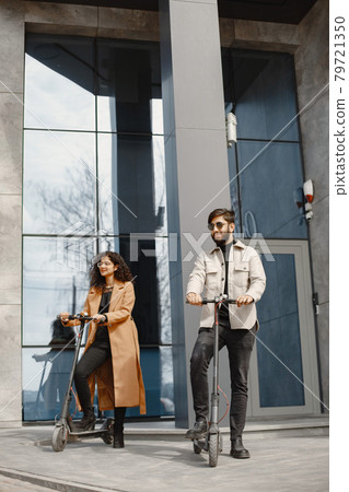 Interracial young couple with scooters in the city background Interracial young couple with scooters in the city background 79721350