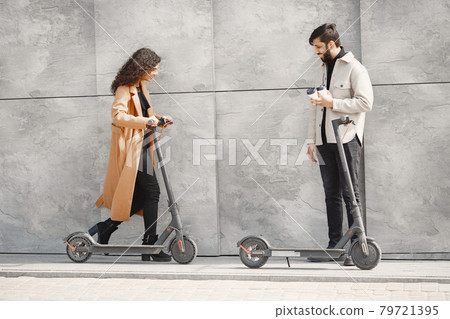 Interracial young couple with scooters in the city background 79721395