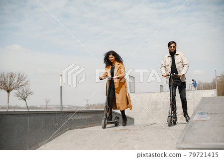 Interracial young couple with scooters in the city background Interracial young couple with scooters in the city background 79721415