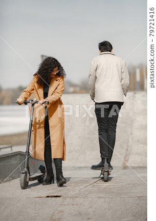 Interracial young couple with scooters in the city background Interracial young couple with scooters in the city background 79721416