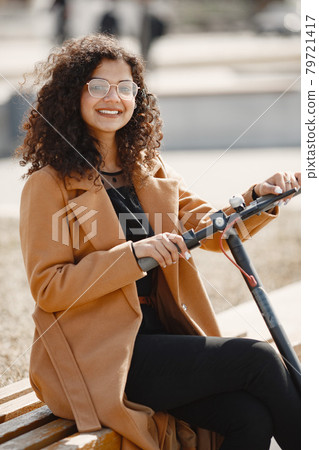 Positive smiling woman riding a kick scooter Positive smiling woman riding a kick scooter 79721417