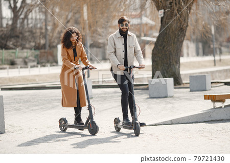 Interracial young couple with scooters in the city background 79721430